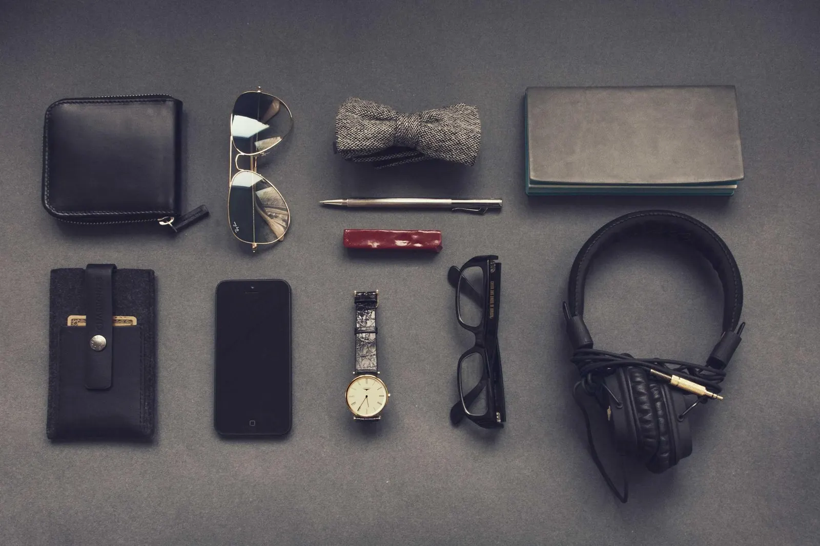 A flatlay of a wallet, watch, glasses and headphones
